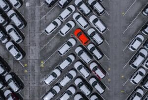A red car parked in a crowded parking lot of white cars, demonstrating the importance of automotive customer acquisition data.